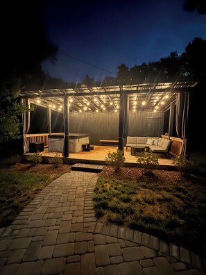 Ein überdachter Außenbereich mit Holz-Pergola, gepolsterten Sitzgelegenheiten und Lichterketten.