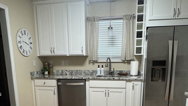A kitchen with white cabinets, a stainless steel refrigerator, a clock, and a window with blinds. - 3 Bedroom Private Lakefront Retreat with Pool, Dock, and Hot Tub (Decatur)
