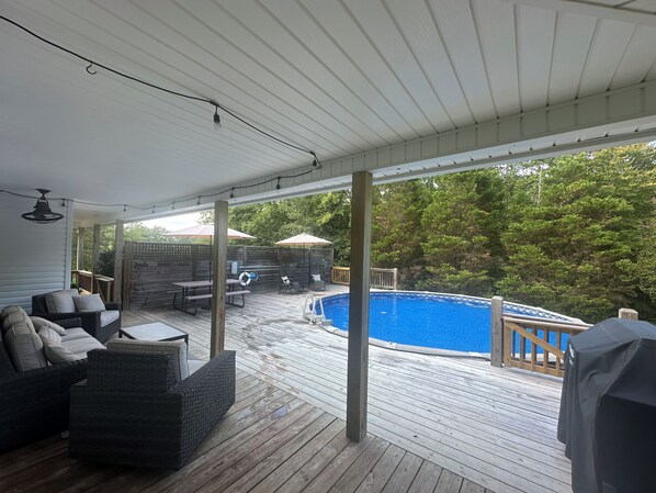 A covered deck with a pool, outdoor furniture, and a wooden fence.