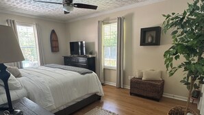 A bedroom with a bed, a dresser, a television, a ceiling fan, a window with curtains, and a plant. - 3 Bedroom Private Lakefront Retreat with Pool, Dock, and Hot Tub (Decatur)