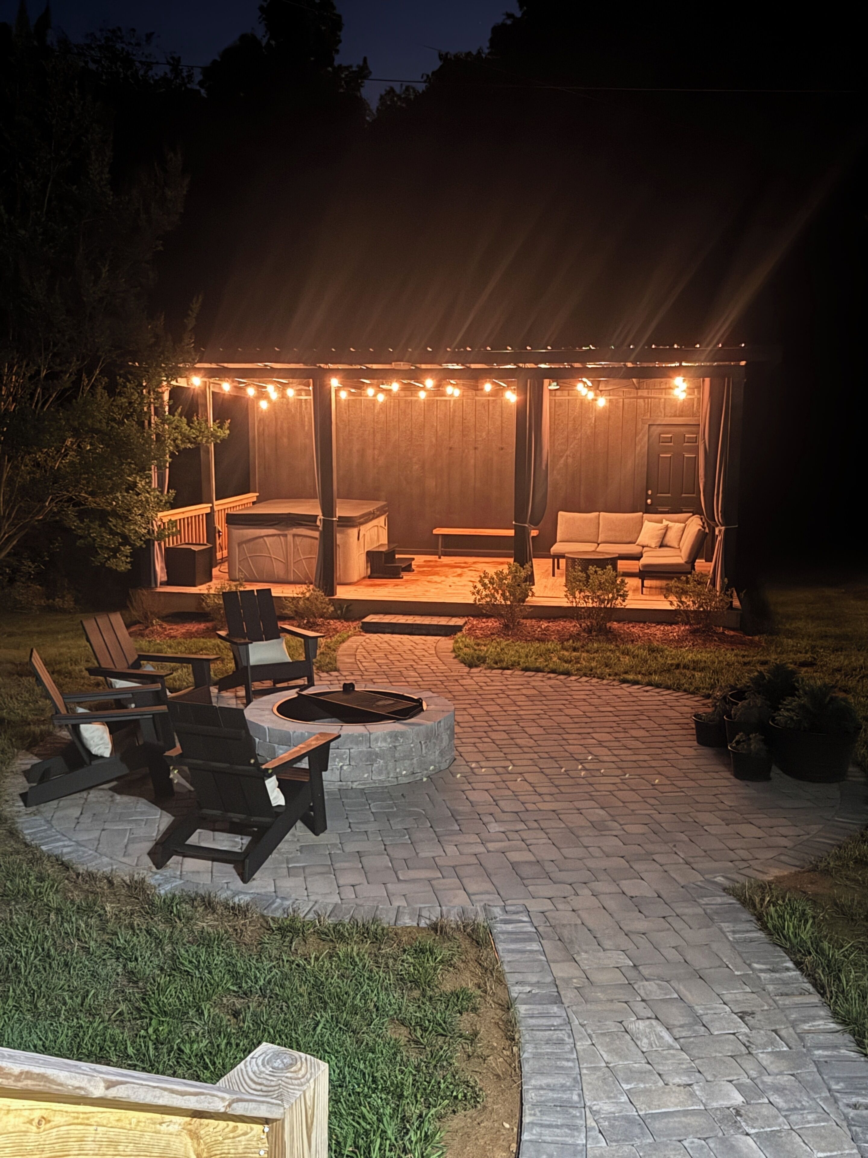An outdoor patio area with a covered seating area, a fire pit, and a wooden deck.