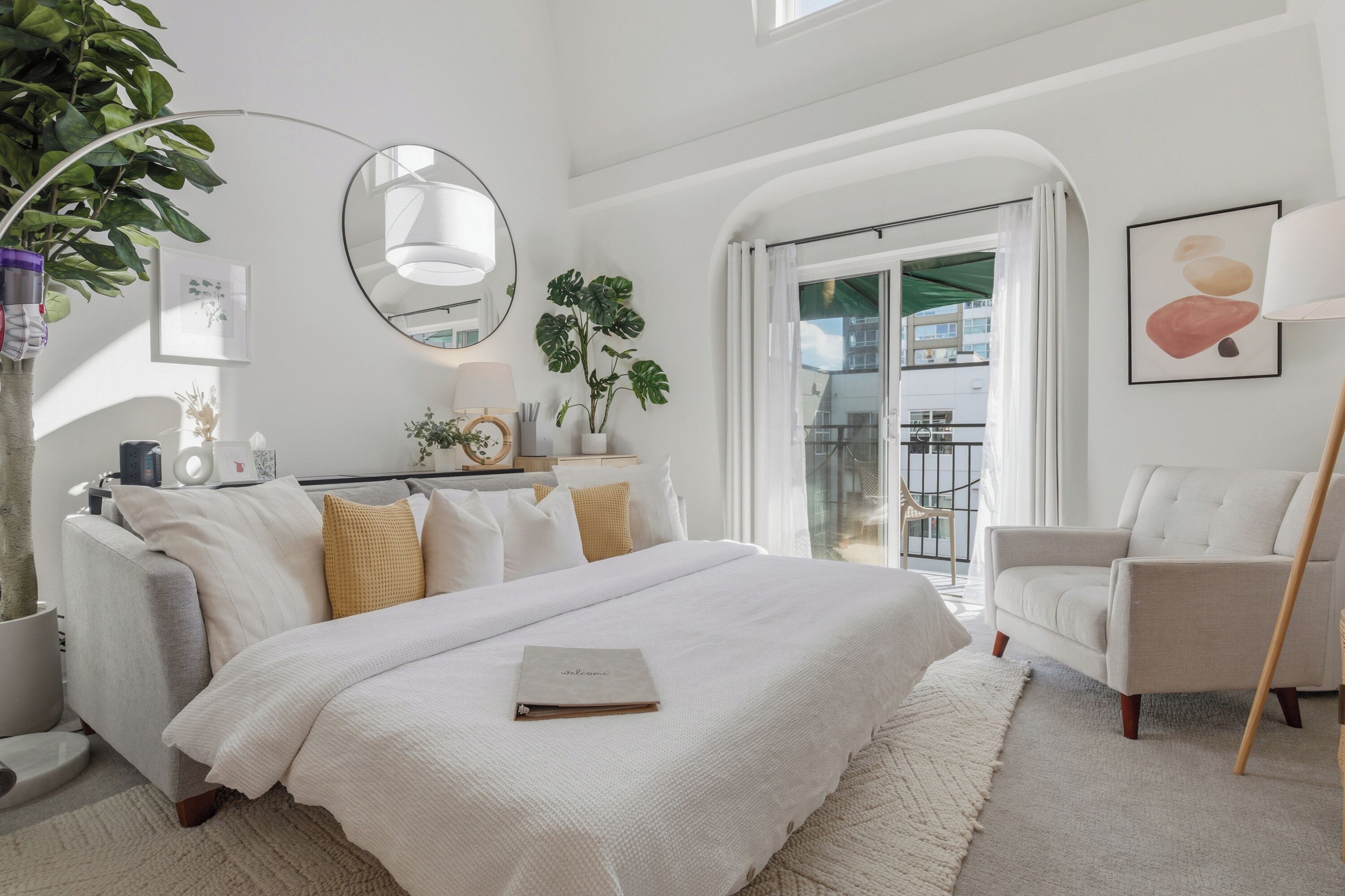 A modern bedroom with a large bed, a bedside table, a chair, a potted plant, and a view of the outside.