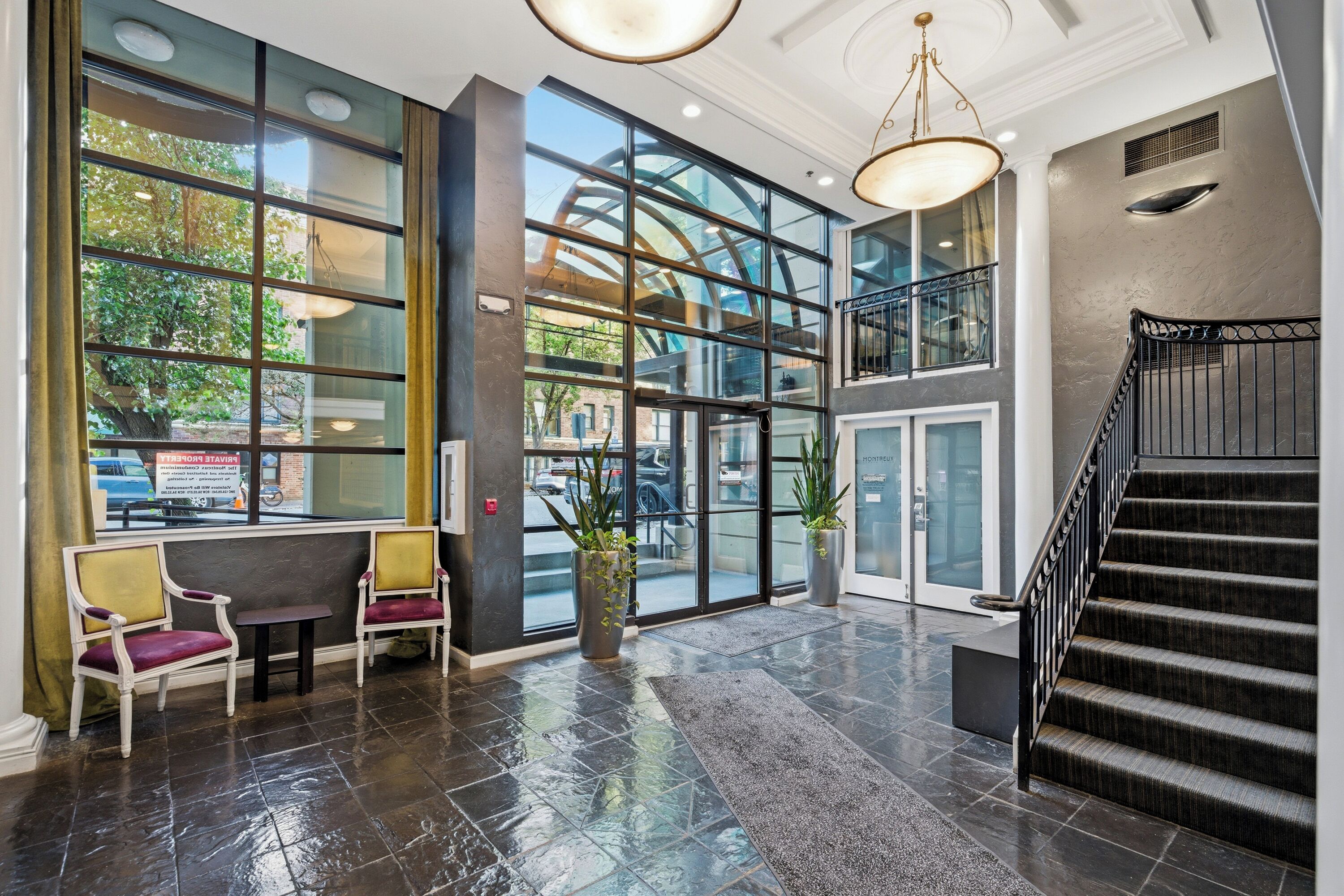 A spacious lobby with a grand staircase, large windows, and a seating area with chairs.