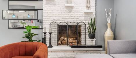 A living room with a white brick fireplace, a sofa, a chair, and a potted plant.