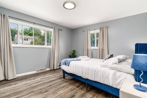 Une chambre à coucher avec un lit, une table de chevet, une lampe et une fenêtre avec des rideaux.