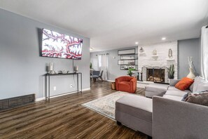 Ein modernes Wohnzimmer mit Flachbildfernseher, grauen Sofas, einem Kamin und Holzboden.