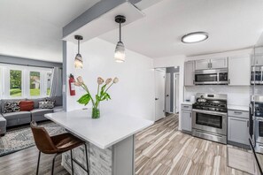 A modern kitchen with stainless steel appliances, a white island, and a seating area with a view. - Modern 5BR Near Downtown & Airport Sleeps 11 (Columbus)