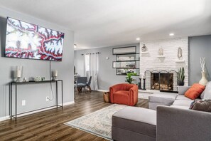 A modern living room with a fireplace, a television mounted on the wall, and a dining area in the background.