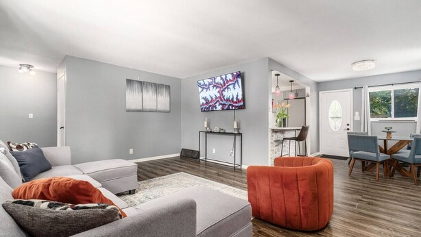 A modern living room with a grey sofa, a red armchair, and a flat-screen TV mounted on the wall.