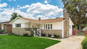 A single-story house with a brick foundation, a white exterior, and a front porch.