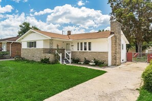 A single-story house with a brick foundation, a white exterior, and a front porch.