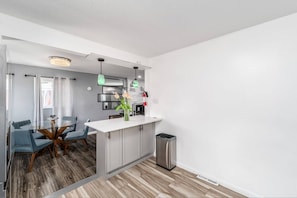 Une cuisine moderne avec un plan de travail blanc, une poubelle en acier inoxydable et un vase avec des fleurs placé sur l’îlot central.