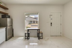 Eine Küche mit Kühlschrank, einem Fenster mit Blick auf ein Gebäude und einer weißen Tür.