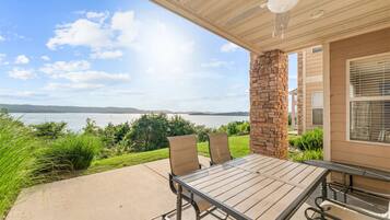 A covered patio with a table and chairs, overlooking a body of water and hills.