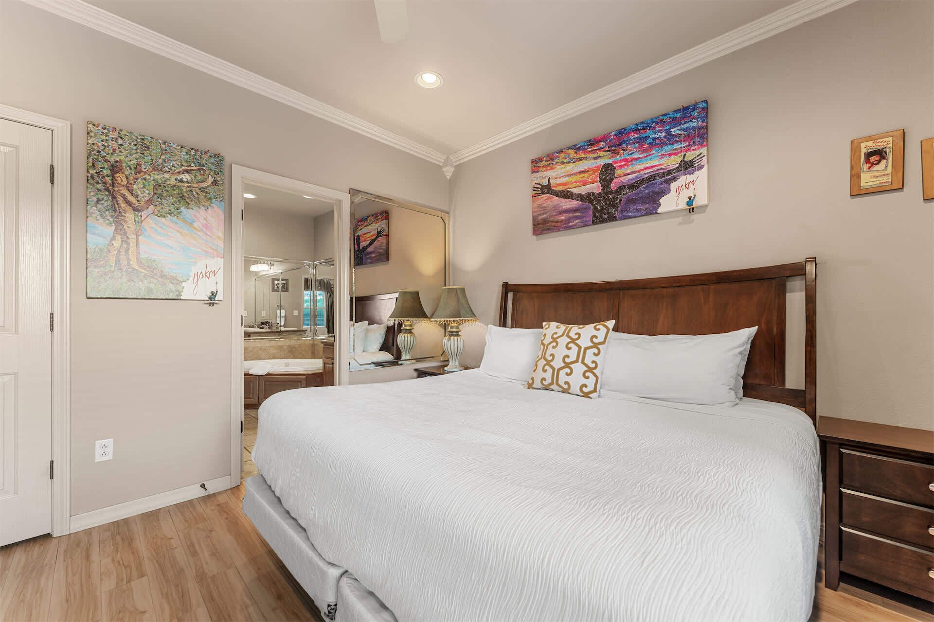 A bedroom with a large bed, a mirror, a nightstand, and artwork on the walls.