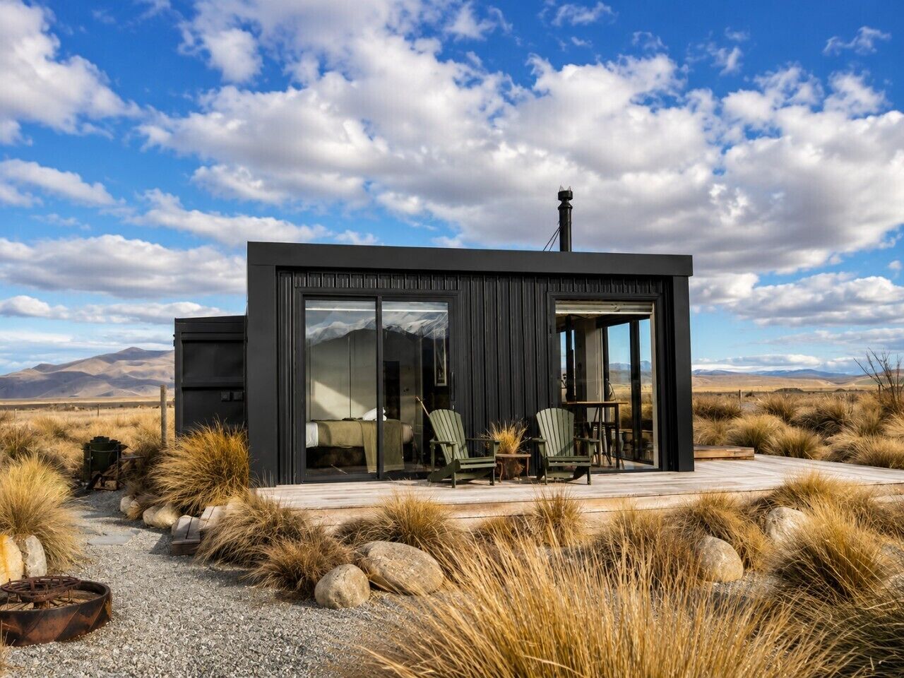 A modern, black building with a glass door and windows, surrounded by dry grass and rocks.