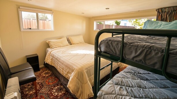 A bedroom with bunk beds, a single bed, a desk, and a patterned rug. - Fabulous Family Stay (Twizel)