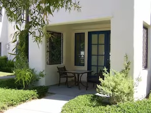 A covered patio with a table and chairs, surrounded by greenery. - Luxury-Remodeled-Pools-Patios, Ground Floor-3 BD 2BA 12 Pools Jacuzzi Views (La Quinta)
