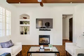 A living room with a fireplace, white sofas, a coffee table, and a TV mounted above the fireplace. - Luxury-Remodeled-Pools-Patios, Ground Floor-3 BD 2BA 12 Pools Jacuzzi Views (La Quinta)