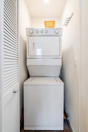 A compact laundry area with stacked appliances, a door, and a wall-mounted rack. - Luxury-Remodeled-Pools-Patios, Ground Floor-3 BD 2BA 12 Pools Jacuzzi Views (La Quinta)