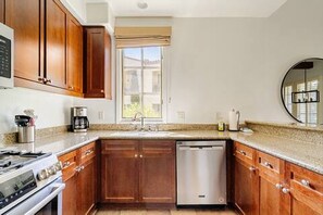 A kitchen with wooden cabinets, a stainless steel dishwasher, and a granite countertop. - Luxury-Remodeled-Pools-Patios, Ground Floor-3 BD 2BA 12 Pools Jacuzzi Views (La Quinta)
