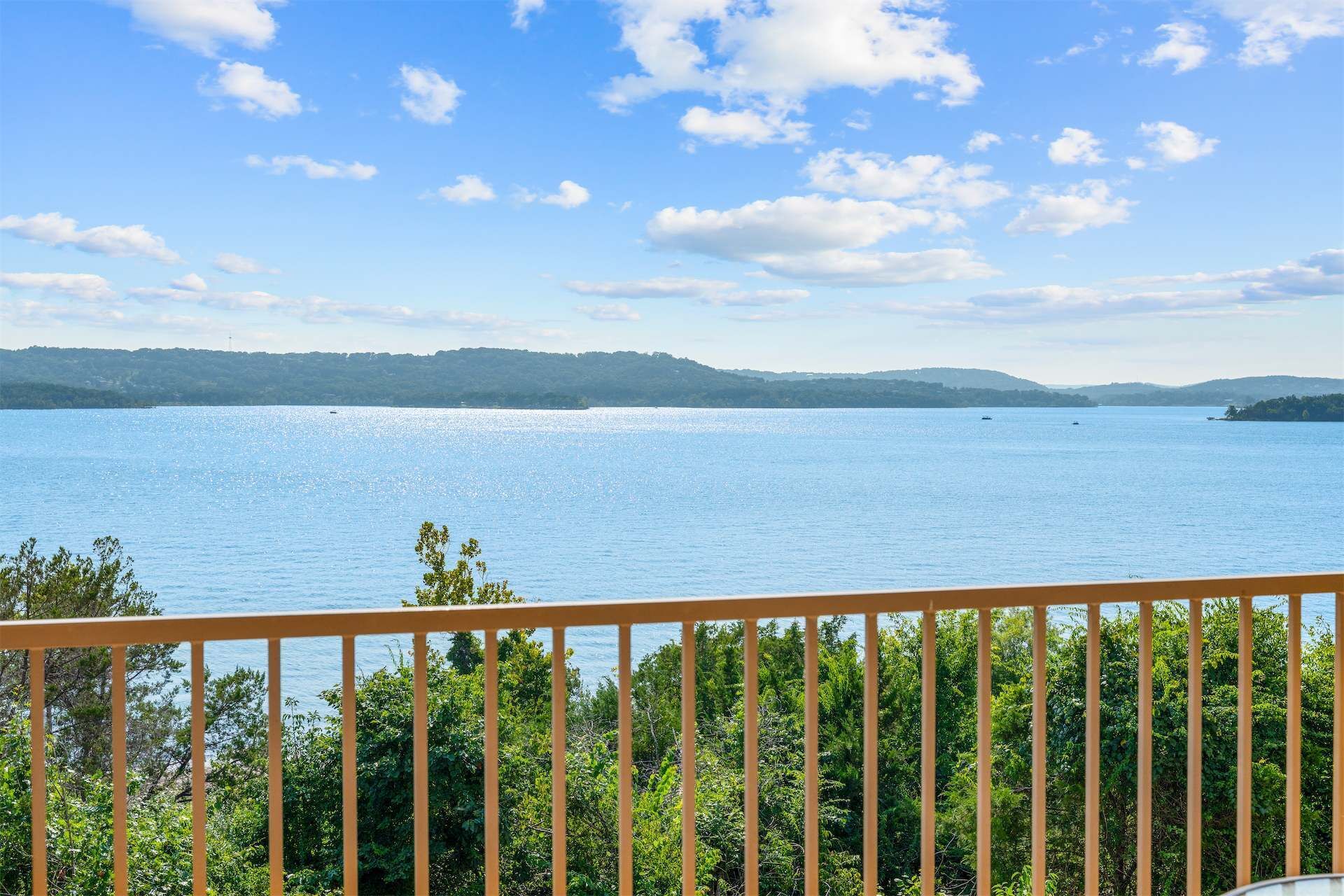 Vista de un lago con baranda de madera al frente, rodeado de follaje.