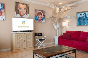 A living room with a red sofa, a coffee table, a television displaying 'GRAND WELCOME BRANSON & THE OZARKS', and wall art. - Smirnoff Pointe - Lakefront (Hollister)