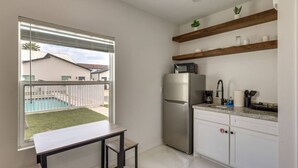 Cuina pràctica amb nevera, microones i un petit taulell. Hi ha una finestra que mostra vistes a una piscina i un edifici a l'exterior.