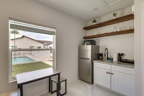 Eine kompakte Küche mit Kühlschrank, Mikrowelle und einer kleinen Arbeitsfläche. Ein Fenster bietet Blick auf einen Swimmingpool und ein Gebäude.