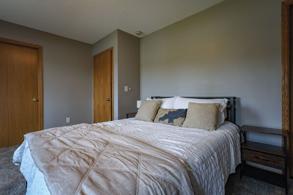 A bedroom with a bed, a nightstand, a wooden door, and a light switch on the wall.