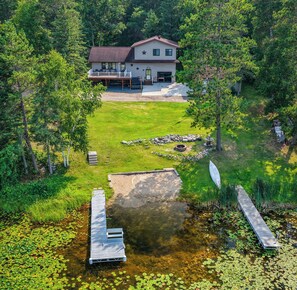 A two-story house with a deck, surrounded by a pond with lily pads and a wooden dock.