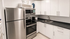 A modern kitchen with stainless steel appliances, a black countertop, and white cabinetry. - Cozy 1-bedroom apartment in  Fort Lauderdale, two blocks from the beach (Fort Lauderdale)