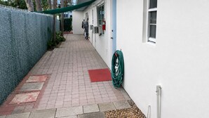 A narrow pathway leading to a building with a blue door, a white wall, and a green hose coiled against it. - Cozy 1-bedroom apartment in  Fort Lauderdale, two blocks from the beach (Fort Lauderdale)
