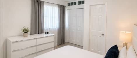 Une chambre à coucher avec un lit, une commode, une porte et une fenêtre avec des rideaux.