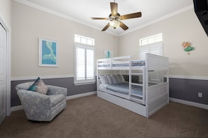 Ein Kinderzimmer mit Etagenbetten, Deckenventilator und Stuhl.