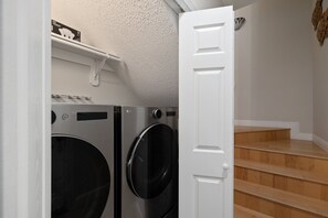 Ein Waschraum mit zwei Frontlader-Waschmaschinen und -Trocknern, einer weißen Tür und einer Holztreppe.