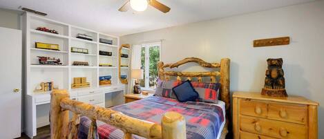 Un dormitorio con estructura de cama de madera, un escritorio con estantes, un aparador y un ventilador de techo.