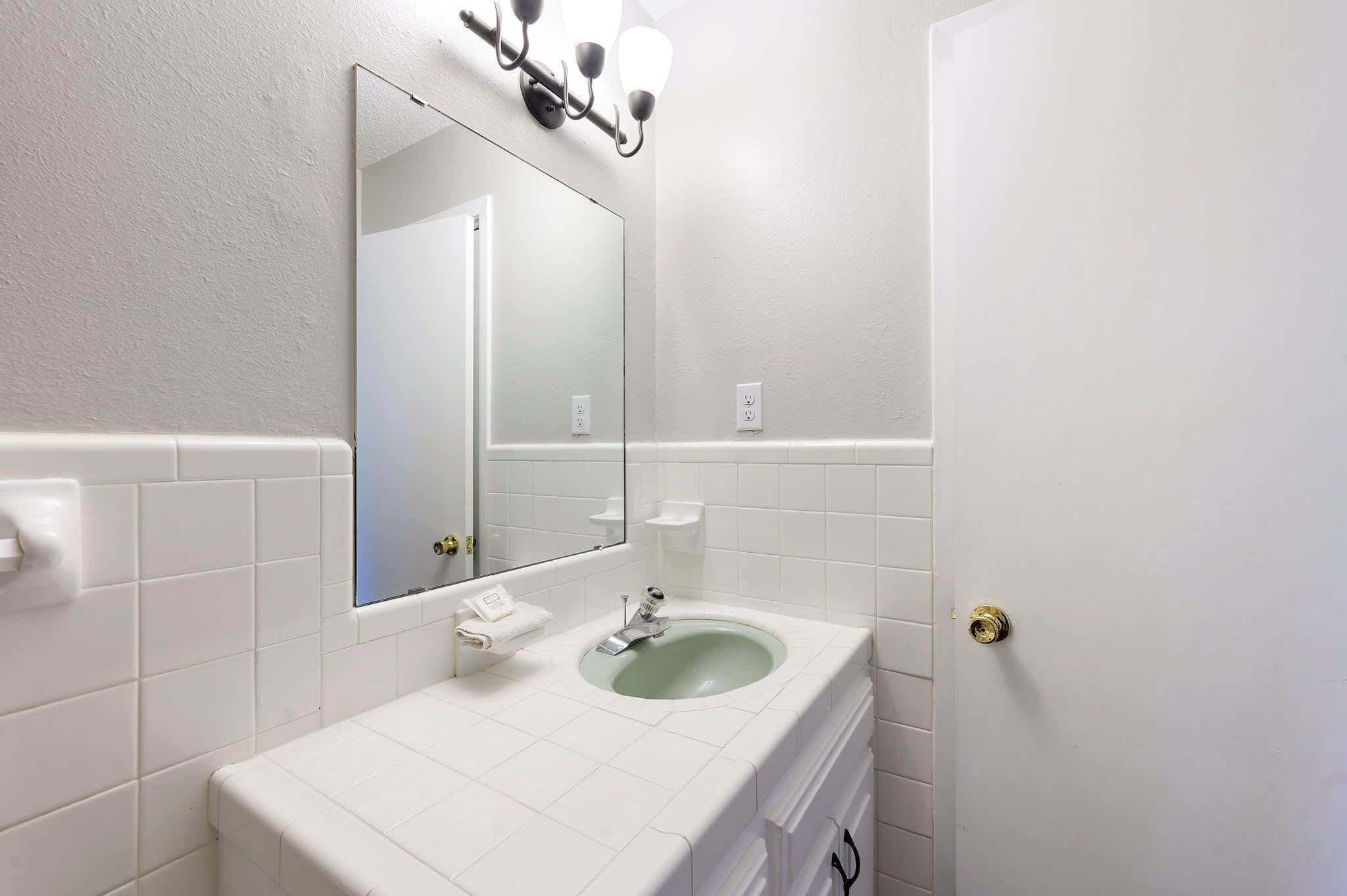 A bathroom with a white sink, a mirror, and a wall-mounted light fixture.