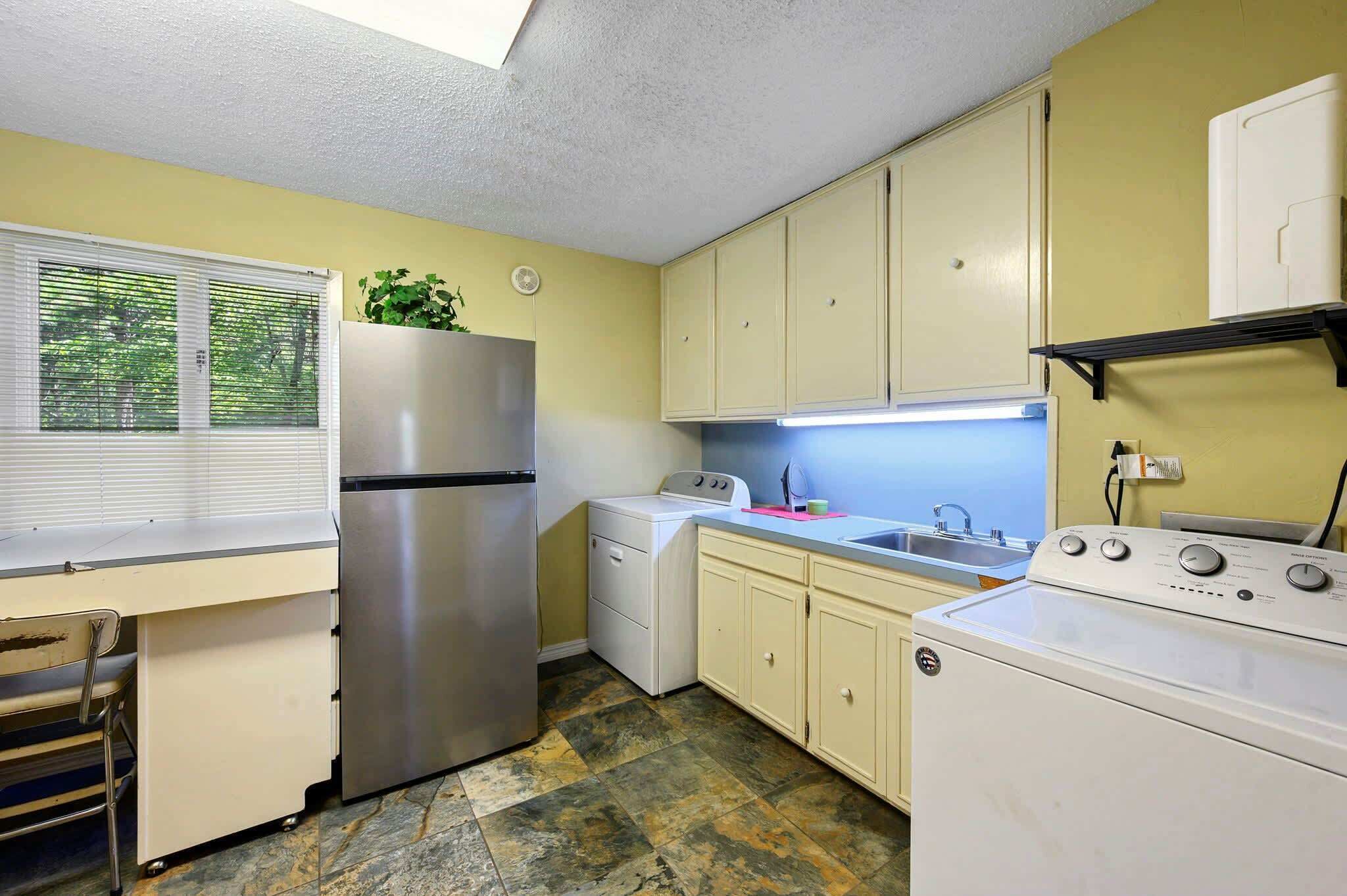 A compact kitchen with a stainless steel refrigerator, a washing machine, and a sink.