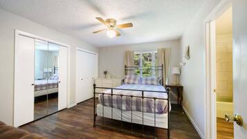 A bedroom with a bed, a ceiling fan, a window with curtains, and a mirror.