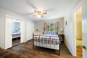Un dormitorio con cama, ventilador de techo, ventana con cortinas y espejo.