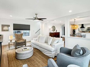 Uma sala de estar moderna com um sofá branco, uma poltrona cinza e uma mesa de centro redonda.