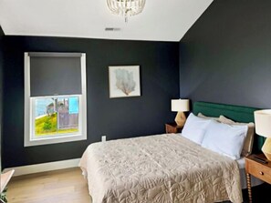 Um quarto com uma cama, uma janela, um quadro na parede e uma mesa de cabeceira com abajur.