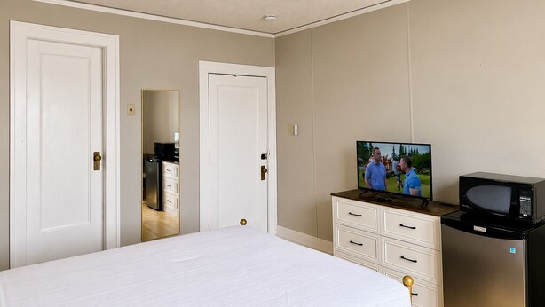 Un dormitorio con cama, televisor, microondas y ventilador de techo.