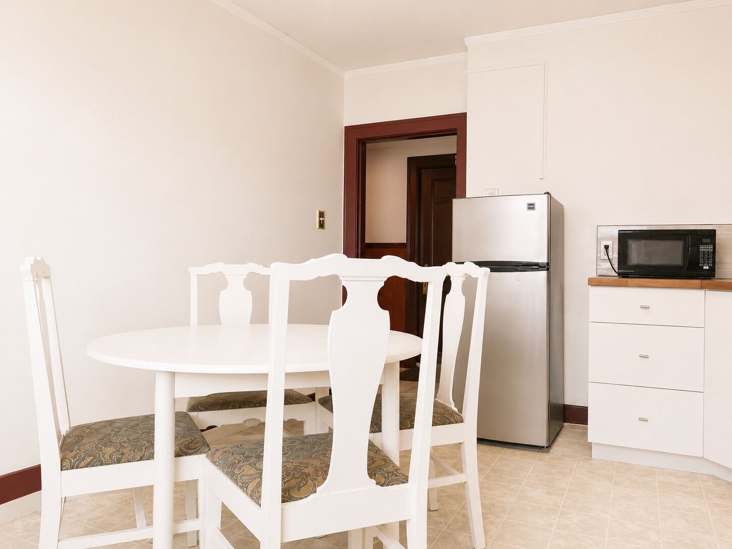 A small kitchen with a white refrigerator, a microwave, and a dining table with chairs.