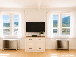 Una habitación con un televisor de pantalla plana grande montado en la pared, un mueble de madera con cajones y dos radiadores en el suelo.