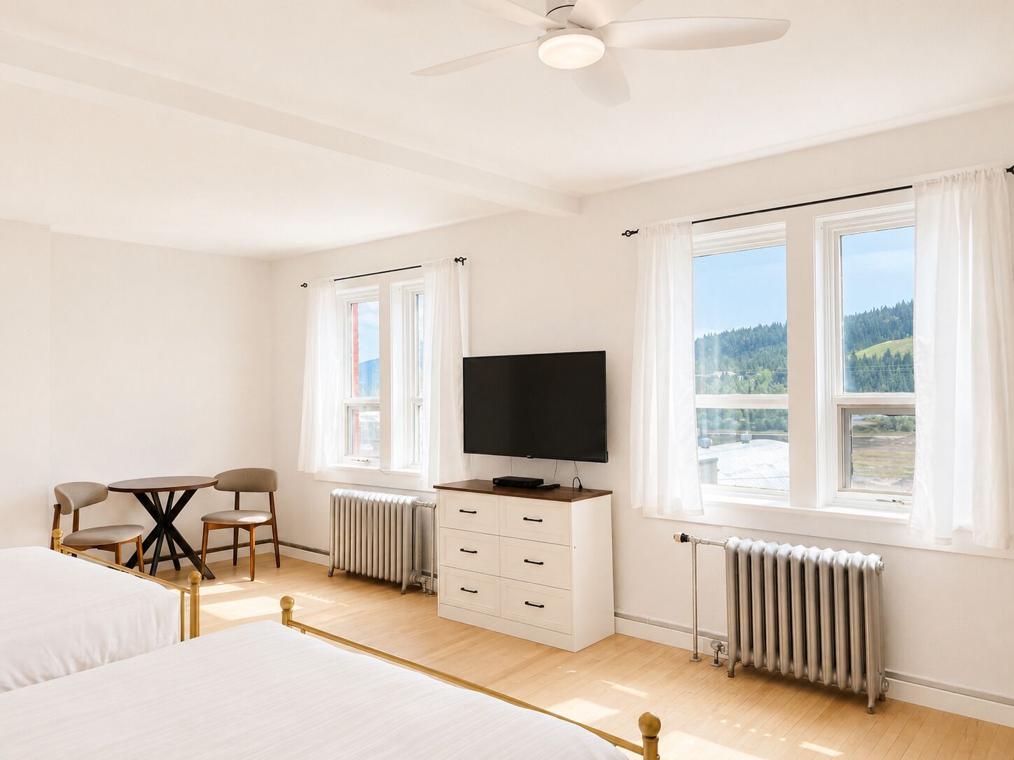 Una habitación de hotel con una cama, un escritorio con silla, un televisor y dos ventanas con cortinas.