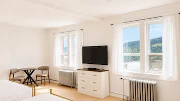 Una habitación de hotel con una cama, un escritorio con silla, un televisor y dos ventanas con cortinas.