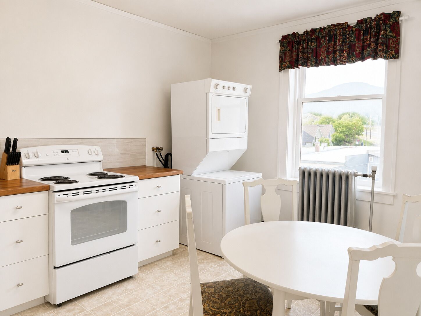 A kitchen with a stove, oven, and a built-in microwave. There is a dining table with chairs and a window with a view.