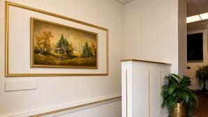 Un pasillo con un cuadro enmarcado, un panel blanco con detalles dorados y una planta en maceta.